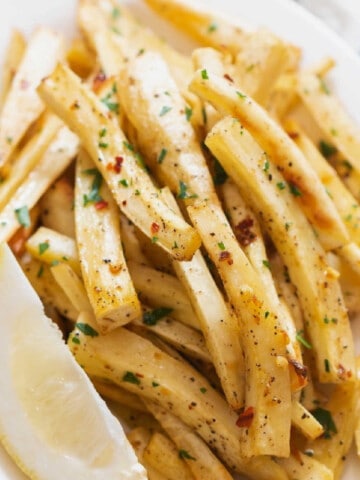 close up view of baked parsnips with parsley and lemon on plate