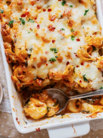 close up view of cheesy baked tortellini pasta with spicy Italian sausage in a casserole dish.