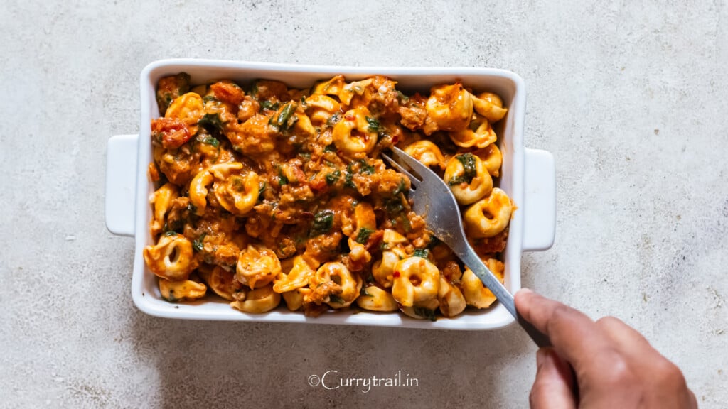 combining cooked tortellini. meat sauce and shredded mozzarella cheese in a casserole dish.