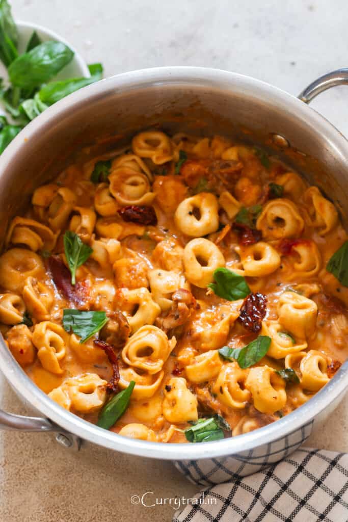 Marry Me chicken tortellini pasta cooked in a pot garnished with fresh basil leaves.