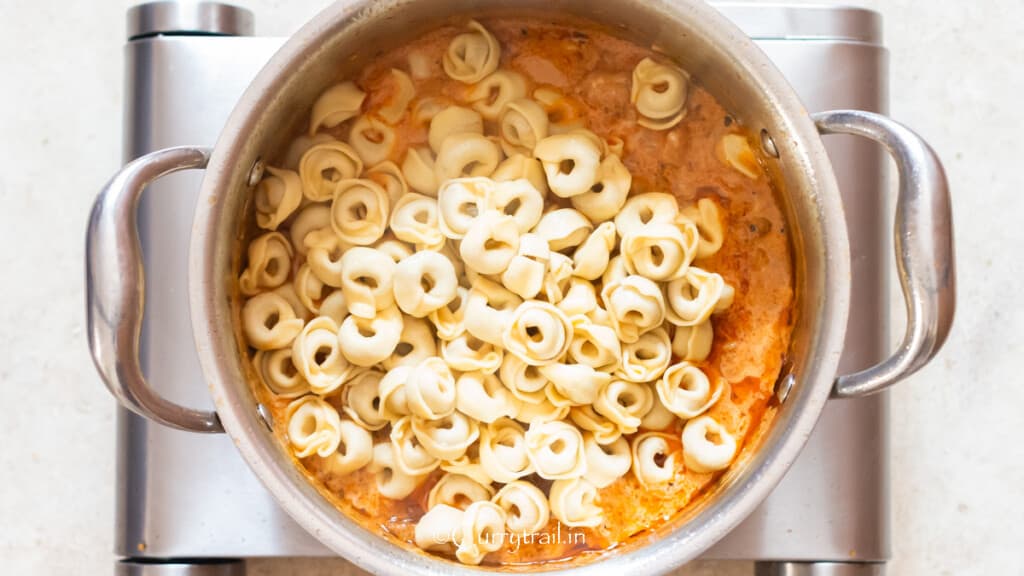 adding cooked tortellini in a creamy tomato-based sauce.