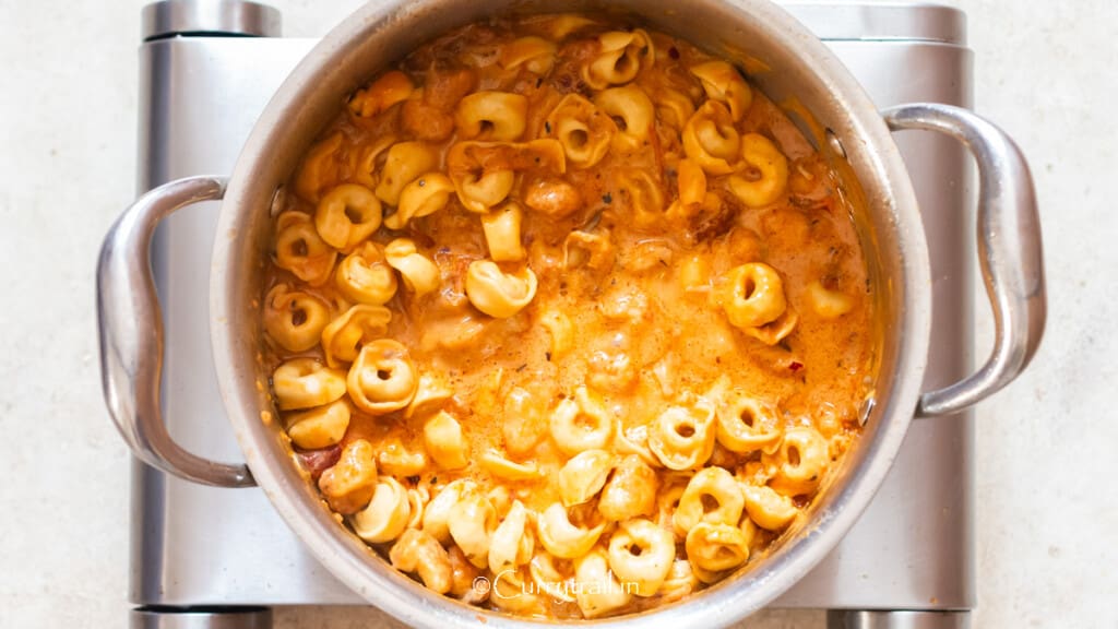 adding cooked tortellini in a creamy tomato-based sauce.