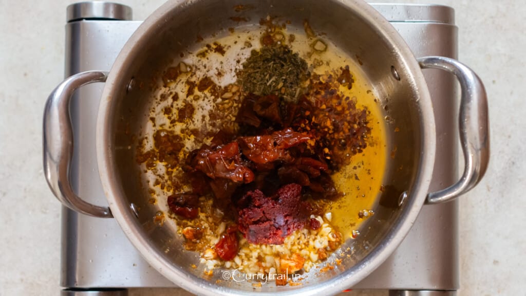 cooking sun-dried tomatoes, tomato paste, and seasoning in a pot.