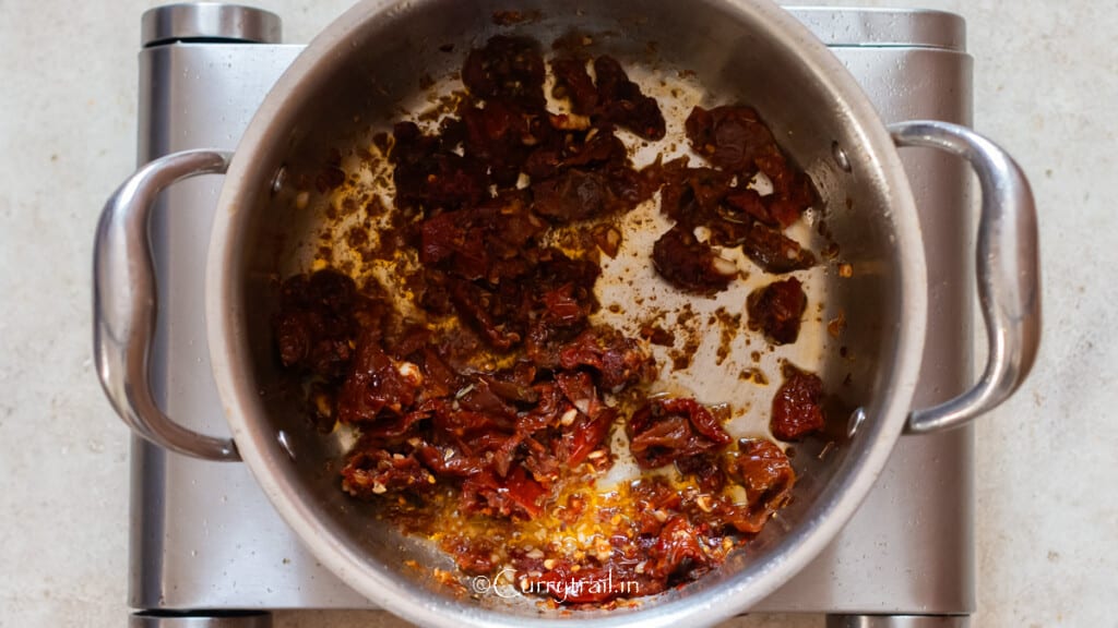cooking sun-dried tomatoes, tomato paste, and seasoning in a pot.