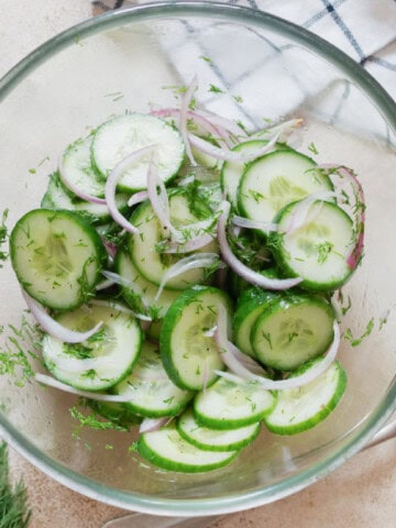 cucumber dill salad in a salad bowl with red onion in it.