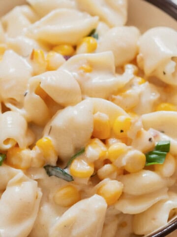creamy sweet corn shell pasta in a bowl with fresh basil leaves sprinkled on top.