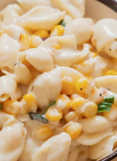 creamy sweet corn shell pasta in a bowl with fresh basil leaves sprinkled on top.