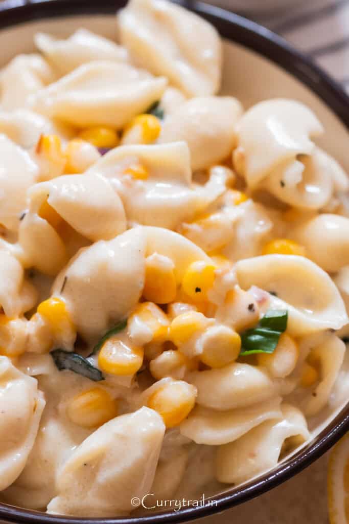 creamy sweet corn shell pasta in a bowl with fresh basil leaves sprinkled on top.