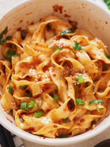 spicy chili garlic noodles in a bowl with scallions and toasted sesame seeds.
