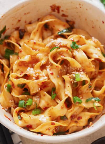 spicy chili garlic noodles in a bowl with scallions and toasted sesame seeds.