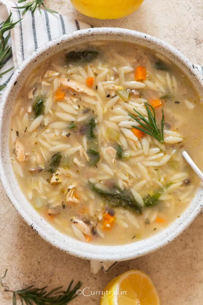 a bowl of lemon chicken orzo soup with lemon and fresh rosemary.