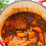Chicken, carrots, and potatoes simmered in tomato-based sauce in a large pot.