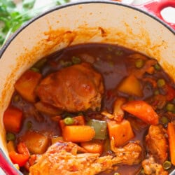 Chicken, carrots, and potatoes simmered in tomato-based sauce in a large pot.