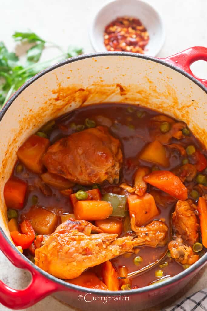 Chicken, carrots, and potatoes simmered in tomato-based sauce in a large pot.