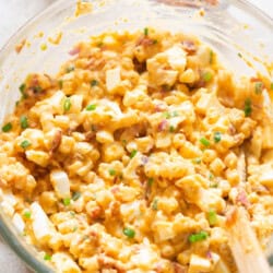 deviled egg pasta salad with green onions sprinkled on top in a mixing bowl.