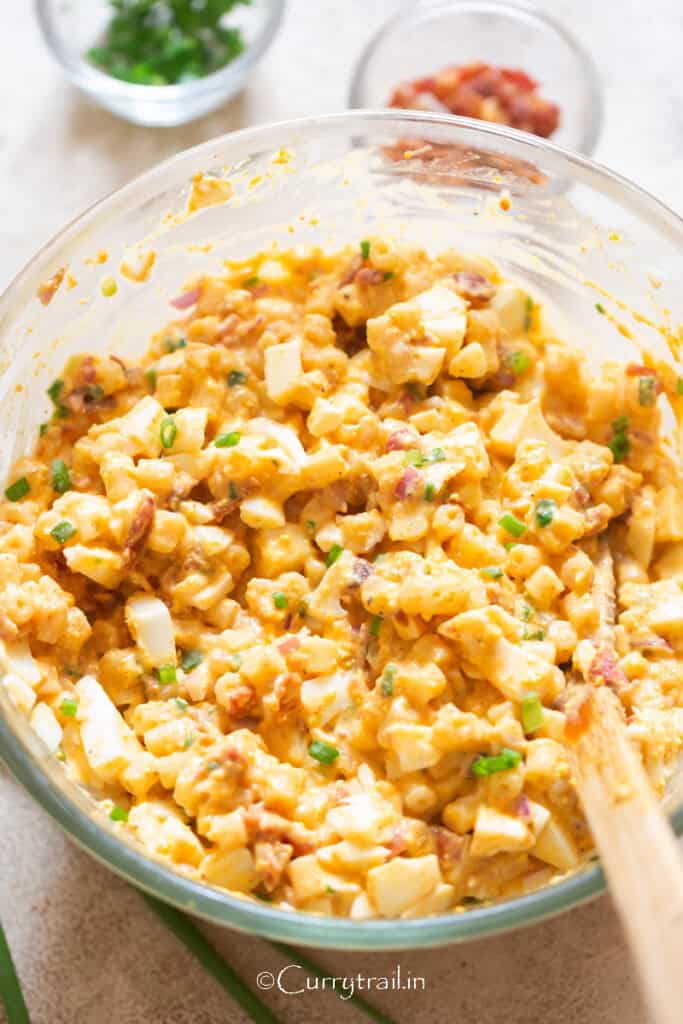 deviled egg pasta salad with green onions sprinkled on top in a mixing bowl.