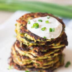 fritters made of zucchini stacked one top of each other with sour cream on top.