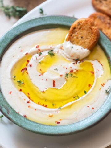 cannellini bean party dip topped with olive oil and fresh thyme, with garlic bread toast on the side.