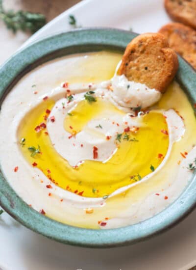 cannellini bean party dip topped with olive oil and fresh thyme, with garlic bread toast on the side.