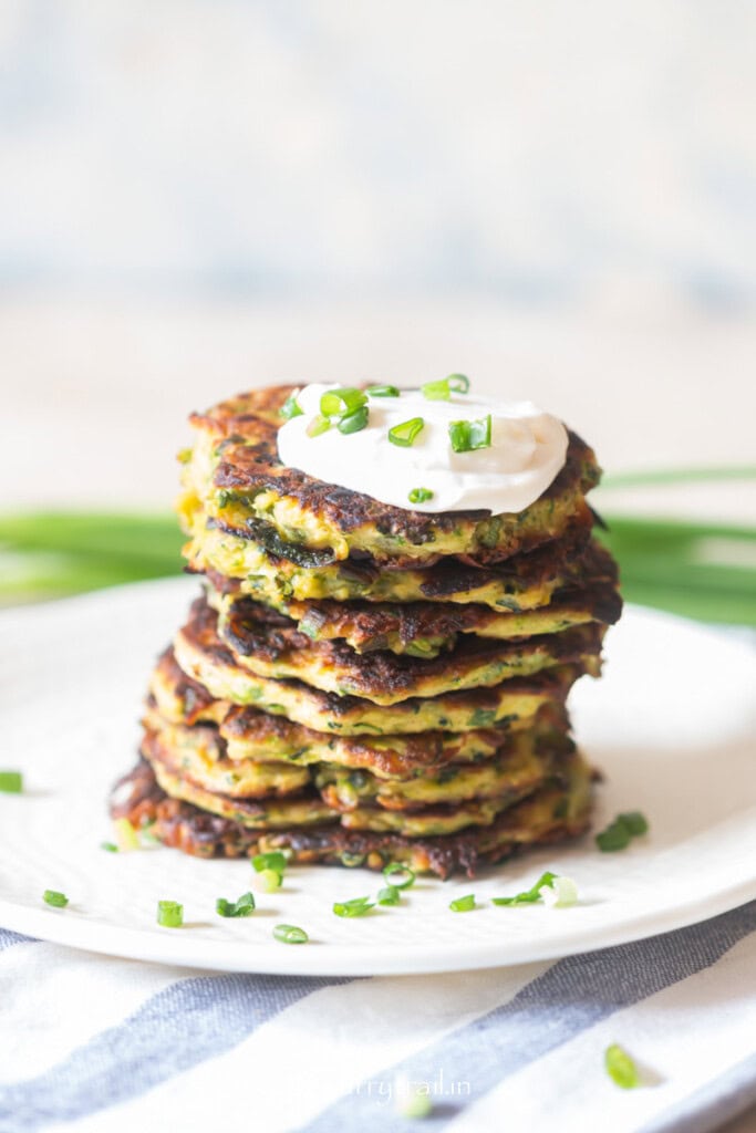 stacks of fritters of zucchini with sour cream on top arranged on a plate.