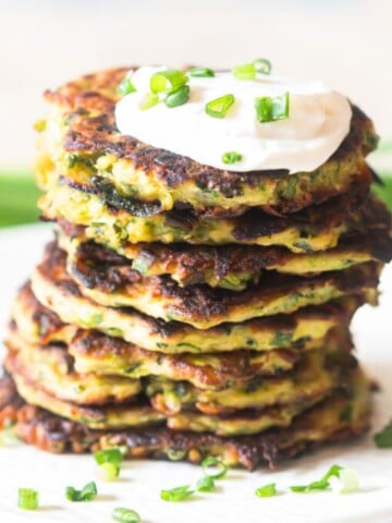 fritters made of zucchini stacked one top of each other with sour cream on top.
