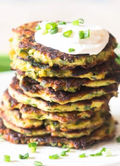 fritters made of zucchini stacked one top of each other with sour cream on top.