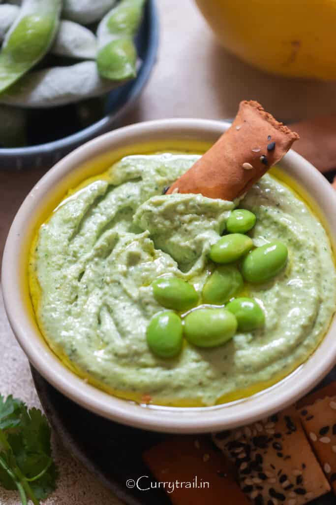 green hummus made with edamame with a cracker dipped in.