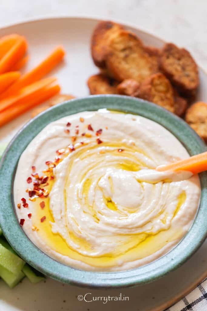 white bean hummus with crackers and vegetable sticks served on the side.