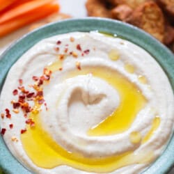 white bean hummus with crackers and vegetable sticks served on the side.