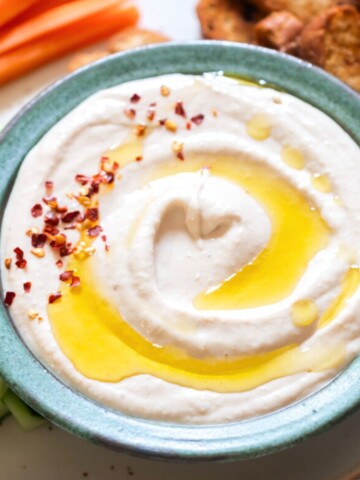 creamy hummus made using white canned beans with olive oil drizzle and red chili flakes sprinkled on top.
