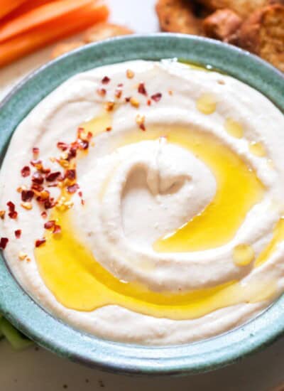 creamy hummus made using white canned beans with olive oil drizzle and red chili flakes sprinkled on top.
