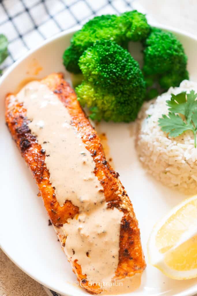 grilled cajun spiced salmon with creamy sauce on top on a plate with cilantro lime rice.