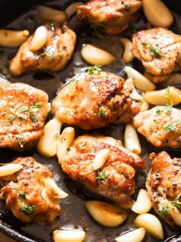 chicken thighs and 40 cloves of garlic cooked in a cast iron pan.