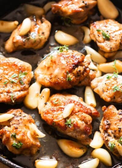 chicken thighs and 40 cloves of garlic cooked in a cast iron pan.