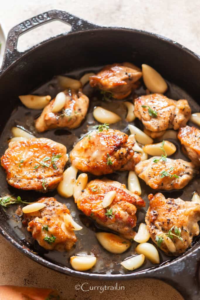 chicken thighs and 40 cloves of garlic cooked in a cast iron pan.