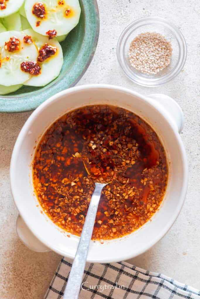 a bowl of chili oil with cucumber salad on the side.