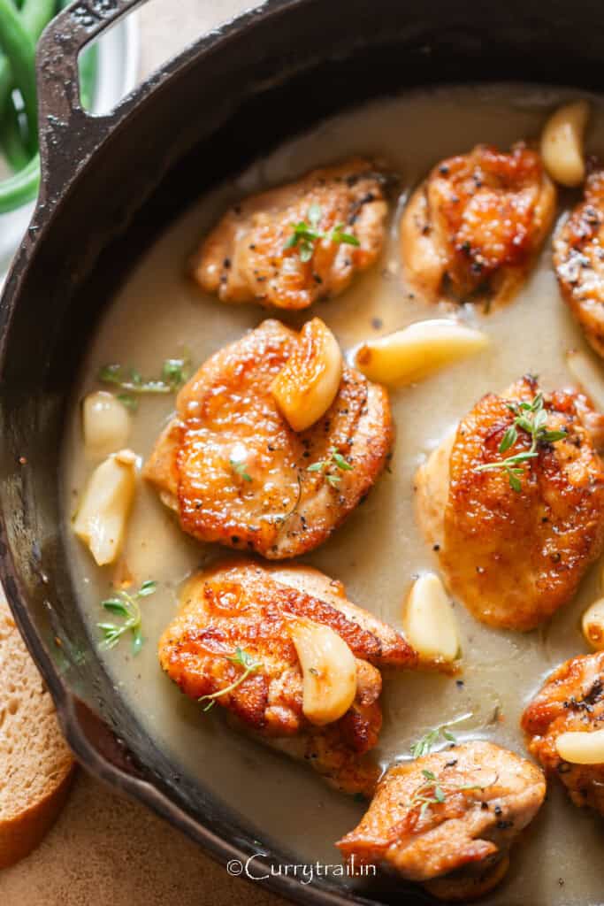 chicken thighs and 40 cloves of garlic cooked in a cast iron pan.