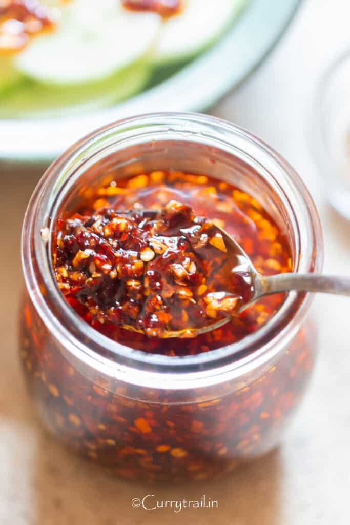 a glass jar of spicy garlic chili oil with spoon.