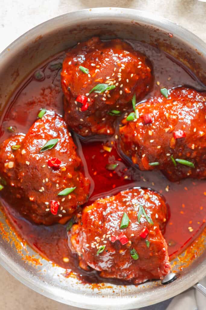 spicy glazed chicken thighs with gochujang sauce cooked in a skillet.