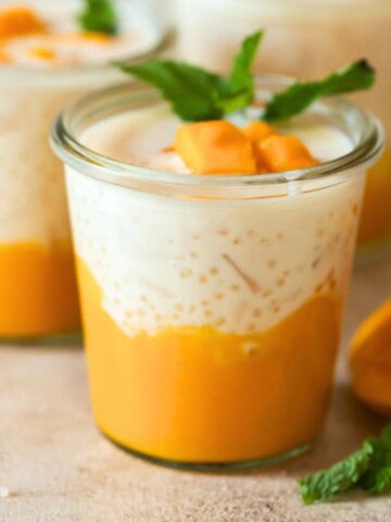 2 glass jars of mango sago served with diced mango and mint leaves.