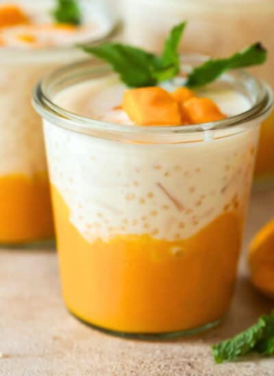 2 glass jars of mango sago served with diced mango and mint leaves.